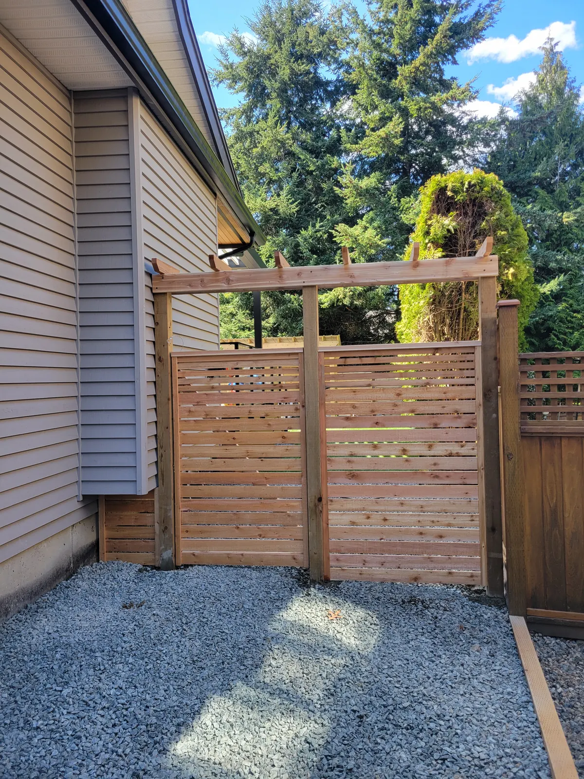 Cedar slat gate with a pergola top beside a house