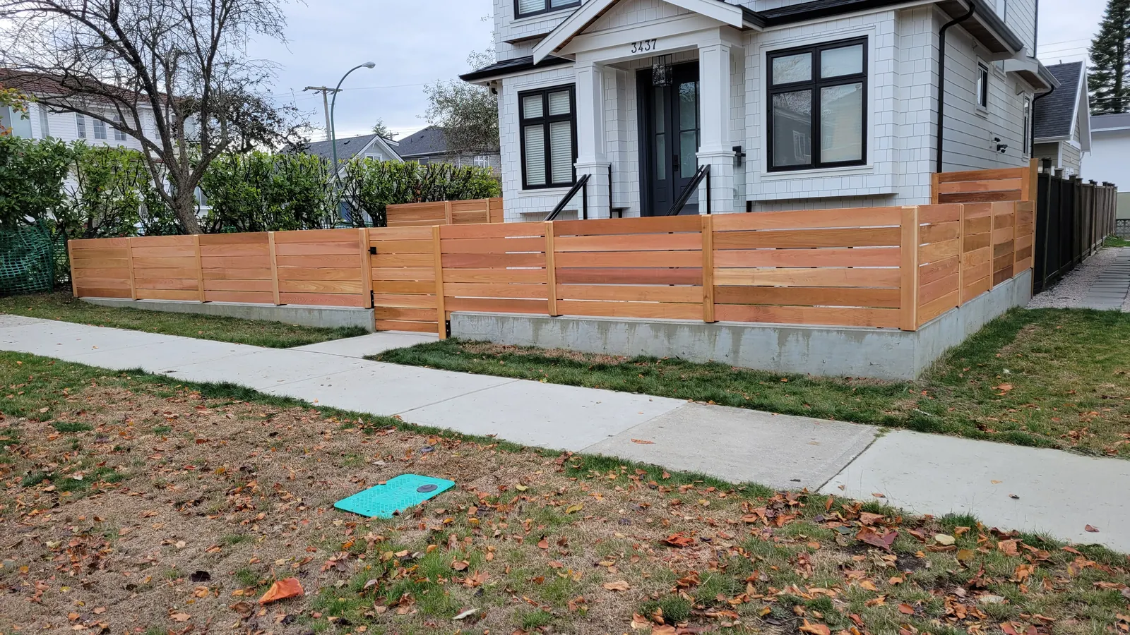 Horizontal cedar front yard fence on a concrete base in front of a white house